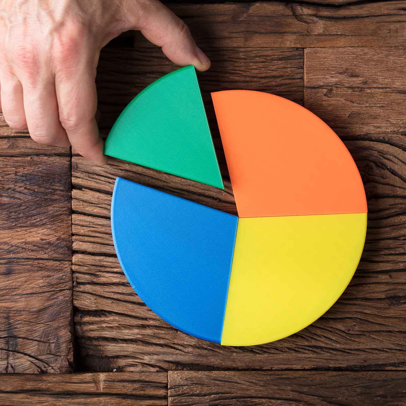 High Angle View Of Businessperson's Hand Placing A Last Piece Into Pie Chart